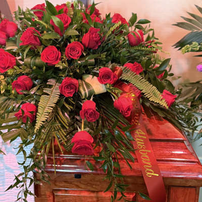 Red rose arrangement on a wooden casket with a red ribbon