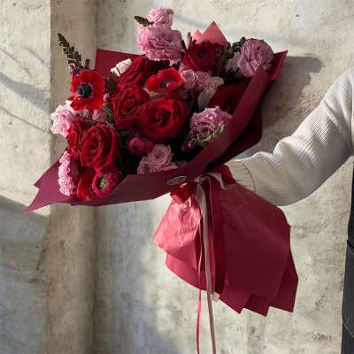 Bouquet of red and pink roses with red anemones wrapped in burgundy paper