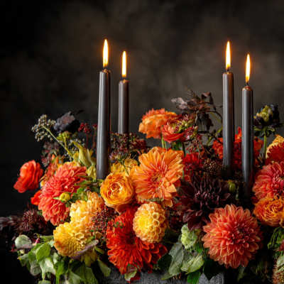 Orange and yellow floral arrangement with lit black taper candles