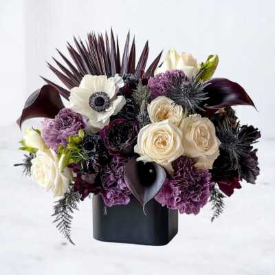 Cream and purple flowers arranged in a black vase with dark foliage