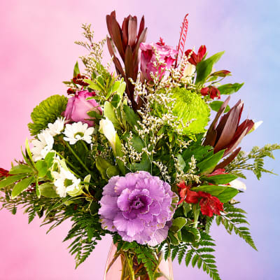 Mixed bouquet of purple, white, red, and green flowers in a glass vase