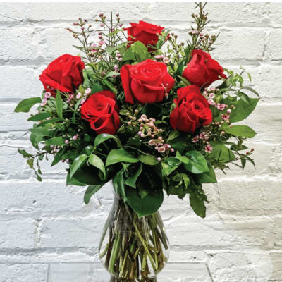 Red roses arranged in a clear glass vase with small pink filler flowers.