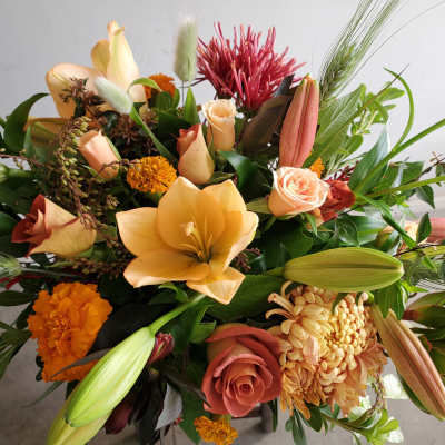Warm-toned arrangement of peach lilies, roses, marigolds, and mums with buds and textural accents