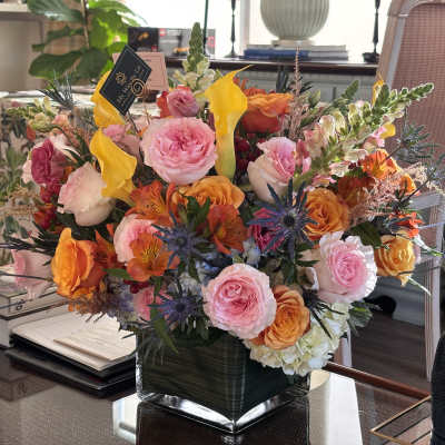 Mixed bouquet of pink, orange, and yellow flowers in a square glass vase