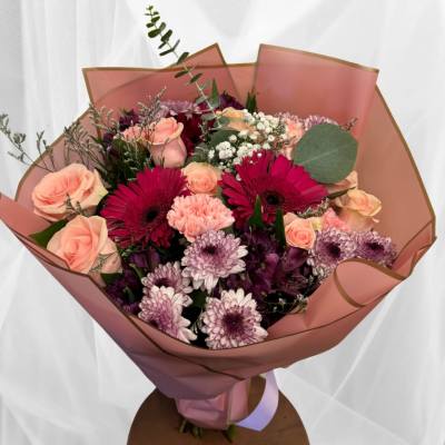 Hand-tied bouquet of pink roses, magenta gerbera daisies and lavender mums in pink wrapping