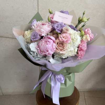 Pastel bouquet of pink, lavender, and white flowers wrapped in green paper