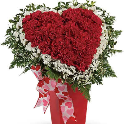 Heart-shaped red carnation arrangement in a red vase with a heart ribbon