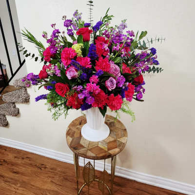 Large mixed bouquet of pink, purple, and red flowers in a white vase