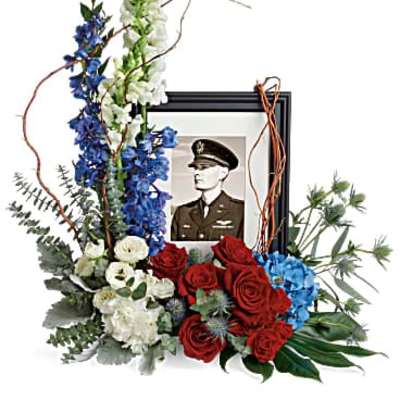 Floral tribute around a framed military portrait with red, white, and blue flowers