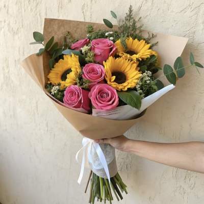 Bouquet of pink roses and yellow sunflowers wrapped in brown paper