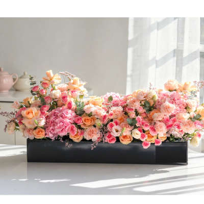 Low rectangular arrangement of pink and peach roses in a black container