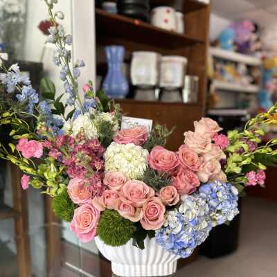 Mixed bouquet of pink roses, hydrangeas, and blue delphinium in a white vase