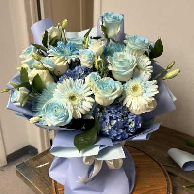 Blue and white bouquet of roses, daisies, and hydrangeas wrapped in lavender paper