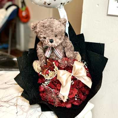 Birthday balloon above a teddy bear and red rose bouquet