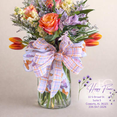 Mixed bouquet in a glass vase with orange roses and tulips, tied with a patterned ribbon.