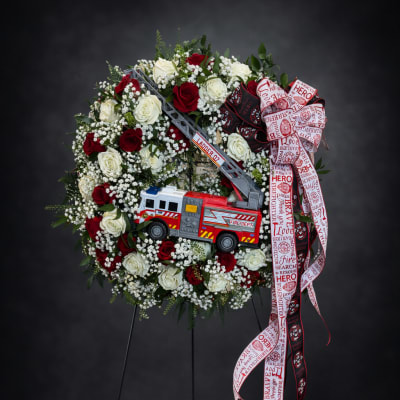 Firefighter-themed rose wreath with a toy fire truck and ribbon on a stand
