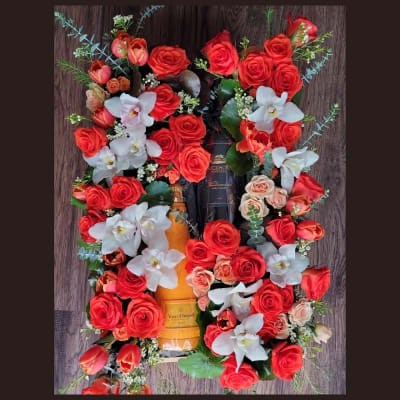 Red roses and white orchids arranged around a champagne bottle