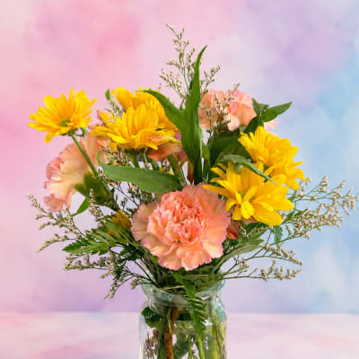 Yellow daisies and peach carnations in a glass jar vase