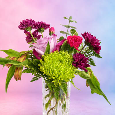 Mixed bouquet of magenta and green flowers in a clear glass vase