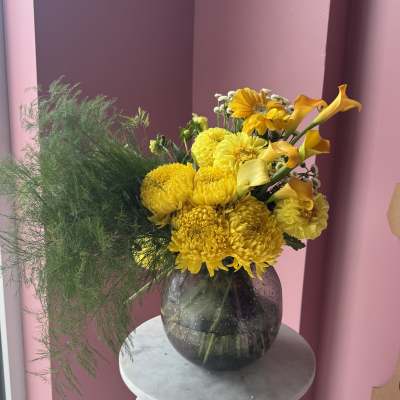 Yellow flowers in a dark glass vase with airy green foliage