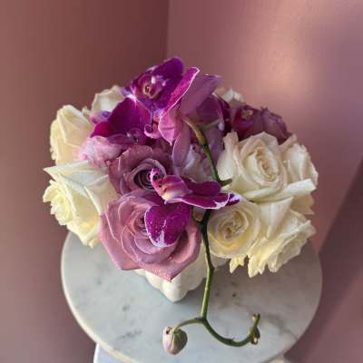 Pink and white roses with purple orchids in a white vase