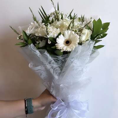 White bouquet with gerbera daisies and roses wrapped in sheer ribboned paper