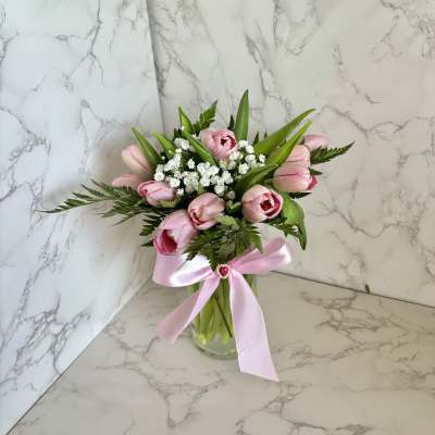 Pink tulips and white filler flowers in a glass vase with a pink ribbon