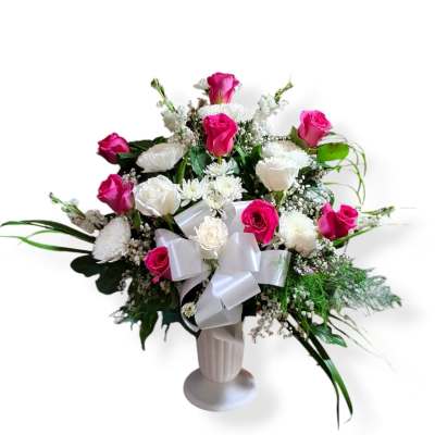 Pink and white rose arrangement in a white vase with a satin bow