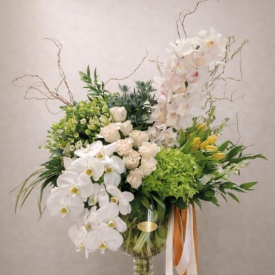 Large white orchid and rose arrangement in a glass vase with orange and white ribbons