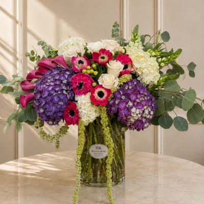 Bouquet of purple hydrangeas, pink anemones, and white roses in a glass vase