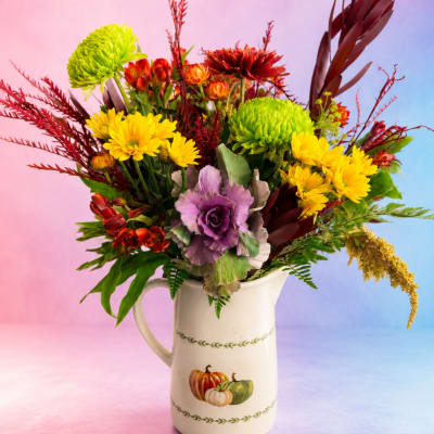 Mixed bouquet in a white ceramic pitcher with yellow, green, purple, and red flowers.