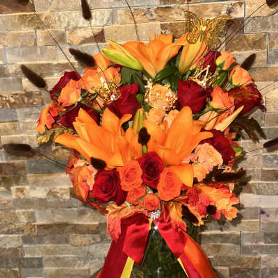Orange lilies and red roses in a glass vase with ribbon and fall leaves