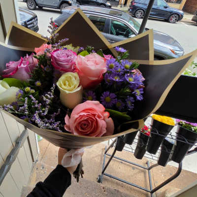 Handheld bouquet of pink, lavender, and white roses with purple filler flowers