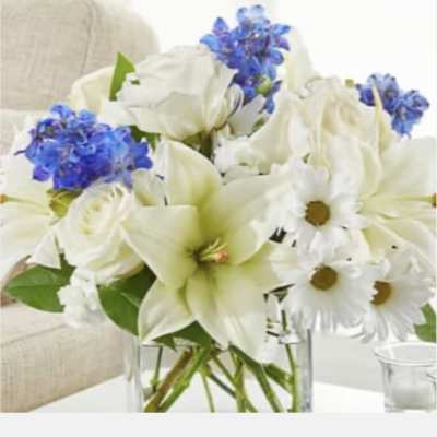White lilies, daisies, and blue flowers in a clear glass vase