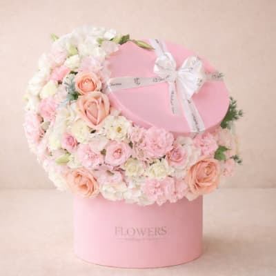 Pink hatbox arrangement with roses and carnations tied with a white ribbon