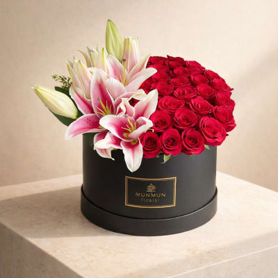 Red roses and pink lilies arranged in a black round box