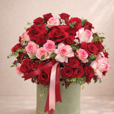 Bouquet of red and pink roses in a round green box with ribbon