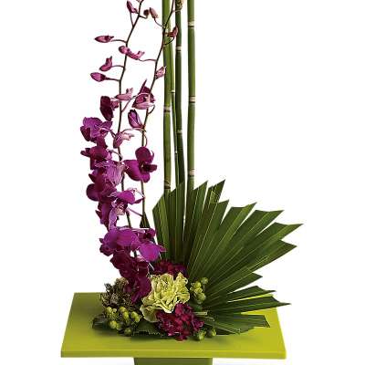 Purple orchid arrangement with bamboo and fan-shaped leaves in a green container