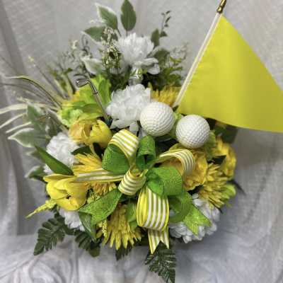 Yellow and white floral arrangement with golf balls and a small flag