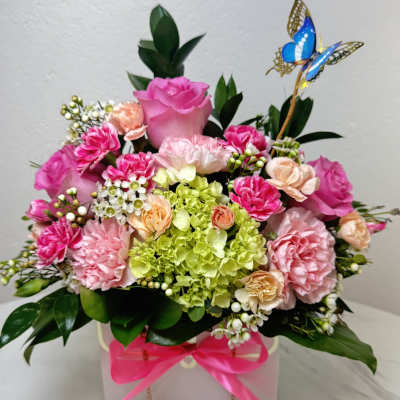 Pink and peach floral arrangement in a white box with a butterfly pick