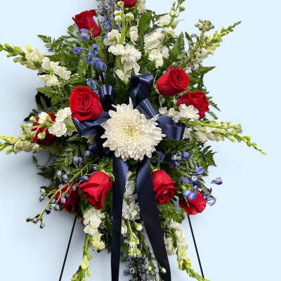 Standing floral spray with red roses, white blooms, and a navy ribbon