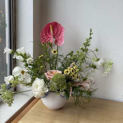 Mixed floral arrangement in a white bowl vase with a pink anthurium and white blooms