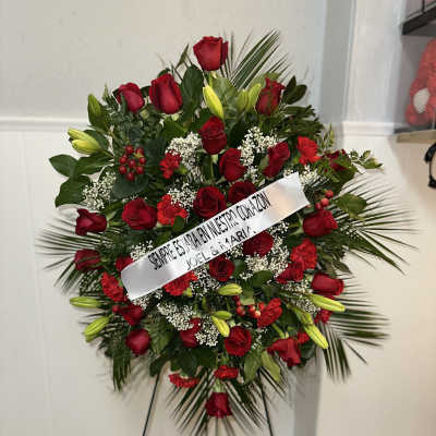 Standing floral spray of red roses and lilies with a white ribbon on an easel