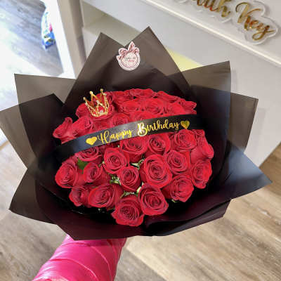 Bouquet of red roses wrapped in black paper with a birthday ribbon and crown topper