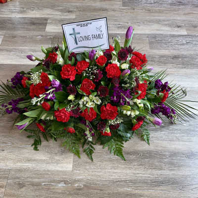 Sympathy floral arrangement with red and purple flowers and a memorial card