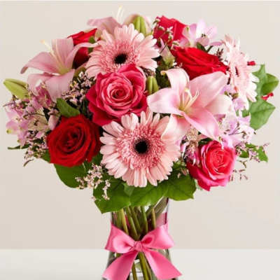 Bouquet of pink and red flowers in a clear glass vase with a pink ribbon