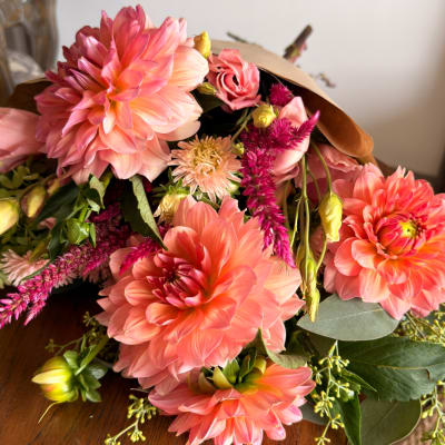 Bouquet of coral-pink dahlias and magenta accent flowers wrapped in brown paper