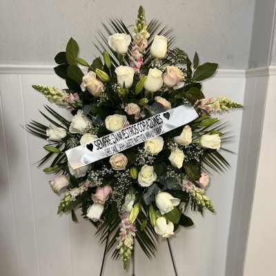 Standing floral wreath of white and blush roses on an easel with a ribbon