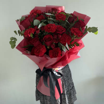 Bouquet of red roses and carnations wrapped in pink paper with a black ribbon