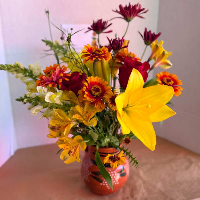 Mixed bouquet with yellow lilies, red roses, and orange daisy-like flowers in a painted vase